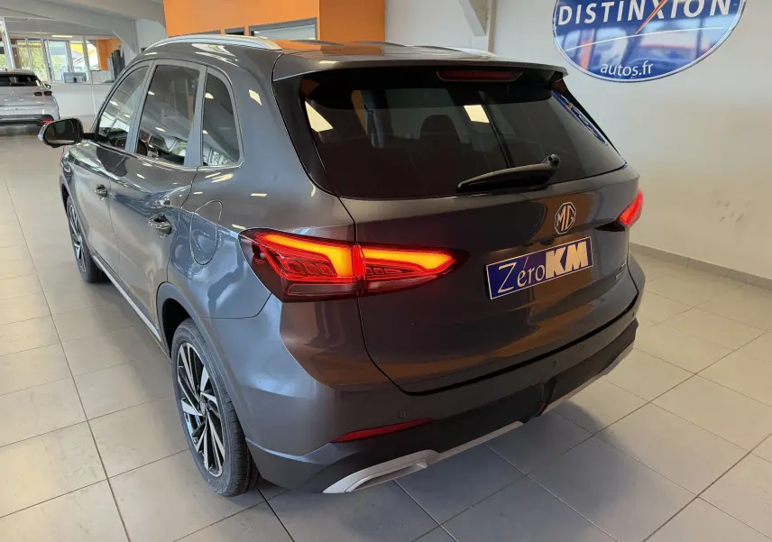 Vue 3/4 arrière droite du MG ZS 1.5 L Hybrid+ gris Candem avec feux LED allumés en showroom.