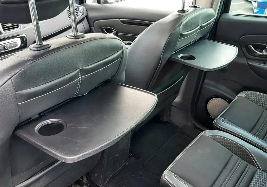 Vue intérieure arrière droite du Renault Grand Scenic noir 7 places, avec tablettes rabattables sur les dossiers des sièges avant.