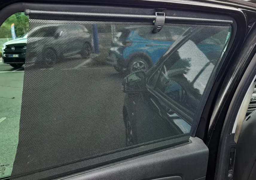 Vue intérieure côté gauche de la porte arrière d'un Renault Grand Scenic noir avec store pare-soleil déployé.