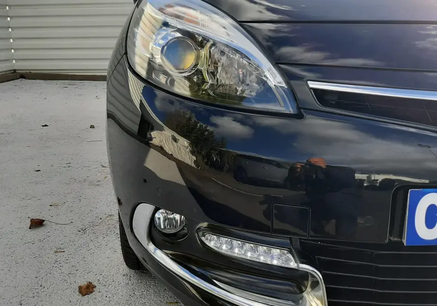 Gros plan sur l'avant gauche noir brillant du Renault Grand Scenic 2015, mettant en valeur le phare et les feux LED.
