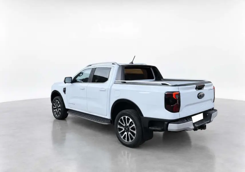Ford Ranger blanc glacier vu en 3/4 arrière droit, avec rideau de benne et jantes alu noires et argentées.