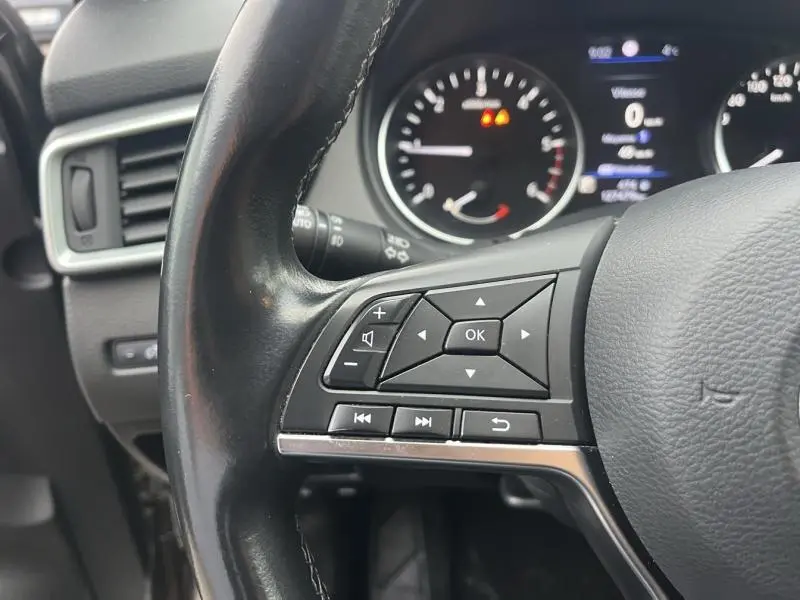 Gros plan sur les commandes multifonctions à gauche du volant cuir du Nissan Qashqai gris Squale, tableau de bord en arrière-plan.