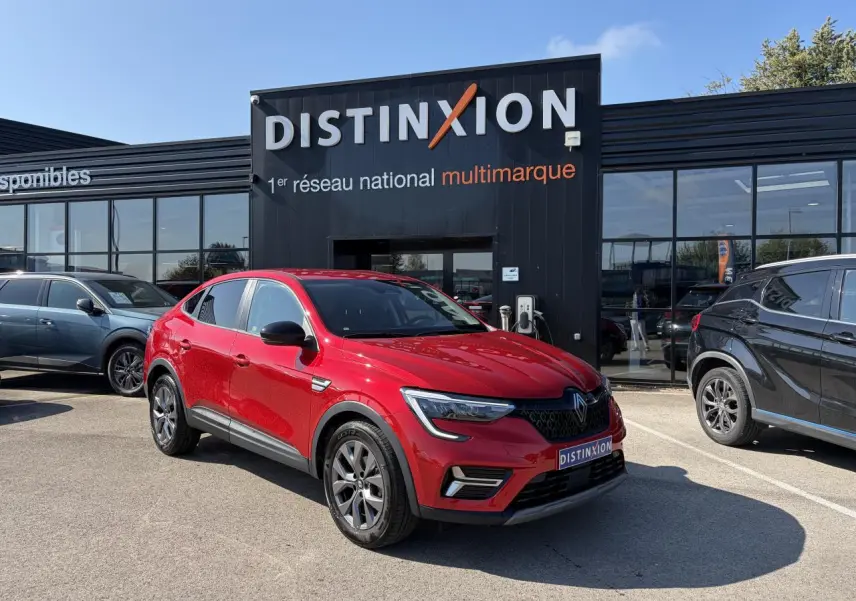 Renault Arkana rouge flamme métal vu en 3/4 avant droit, avec jantes alliage grises 17 pouces, stationné devant un showroom.