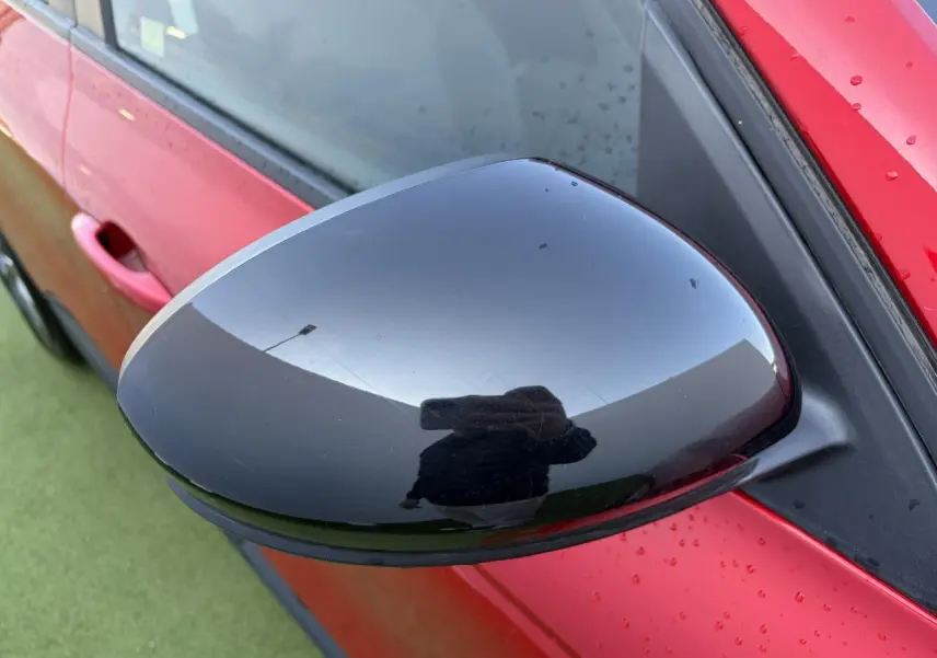 Rétroviseur noir brillant côté gauche d’un Renault Arkana Rouge Flamme Metal avec portière et poignée visibles.