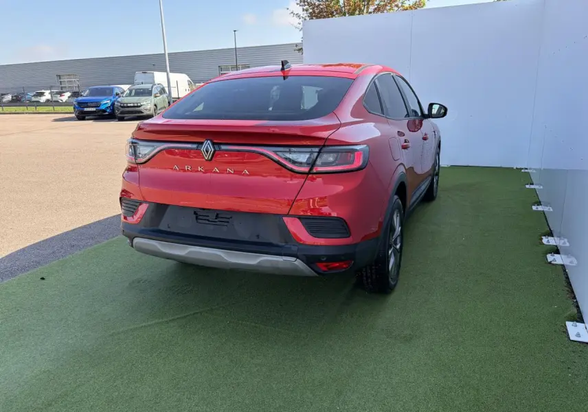 Vue 3/4 arrière droite d'une Renault Arkana rouge flamme métal avec feux arrière LED et jantes alliage grises sur sol vert.