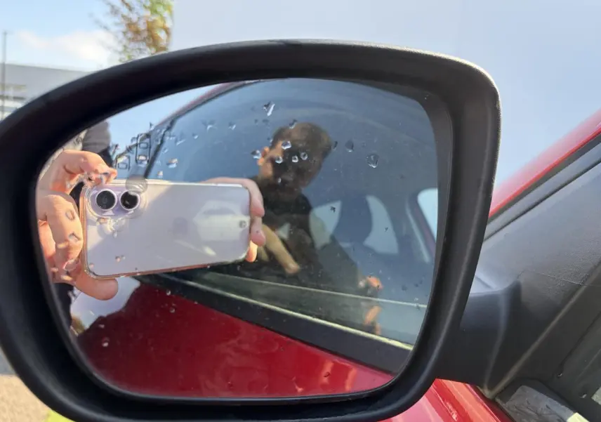 Rétroviseur extérieur côté gauche d’un Renault Arkana rouge flamme métal avec reflet partiel de la portière et d’une personne.