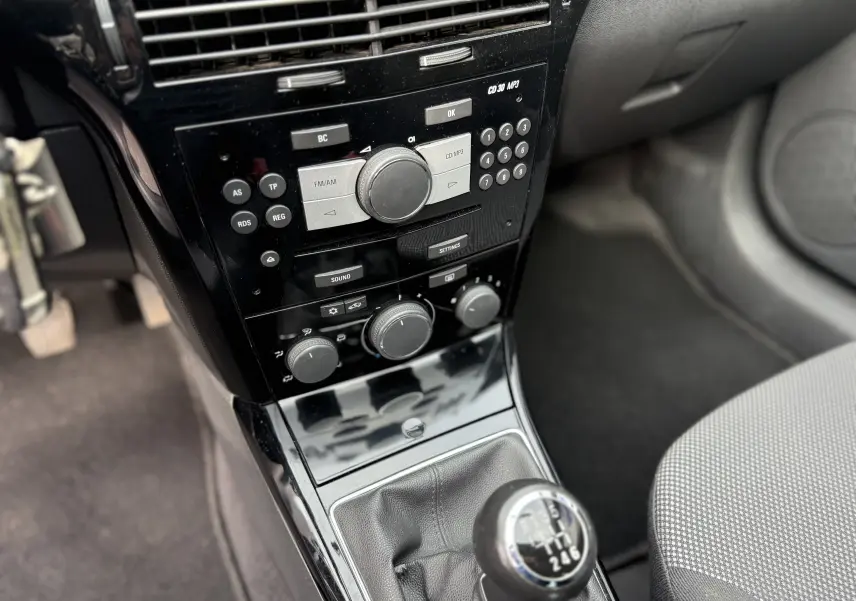 Gros plan sur la console centrale noire et le levier de vitesses manuel de l'Opel Astra gris, avec commandes radio et climatisation visibles.
