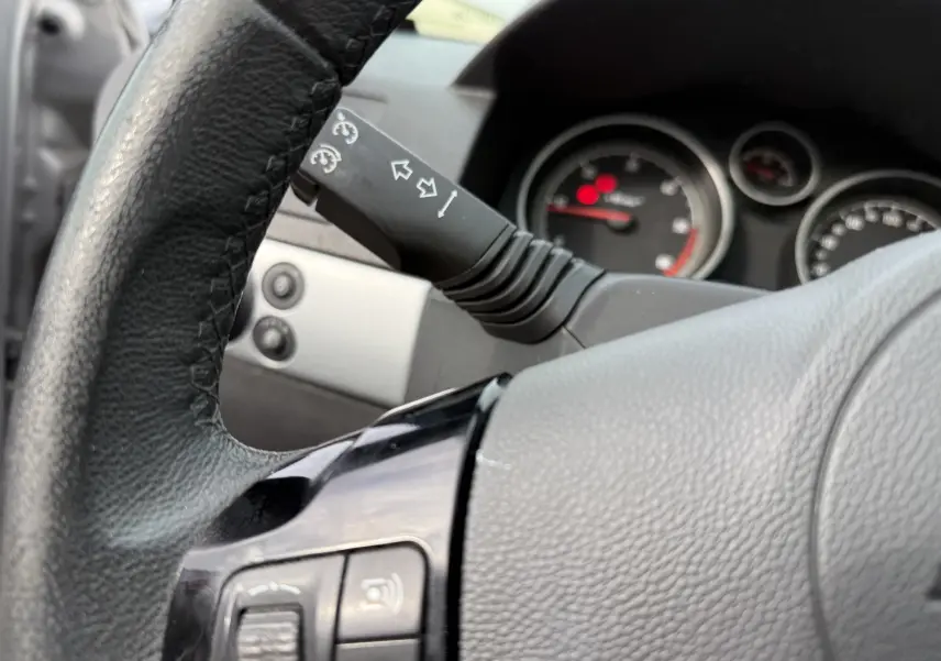 Gros plan sur le volant en cuir noir et la commande de clignotants d'une Opel Astra gris, tableau de bord en arrière-plan flou.