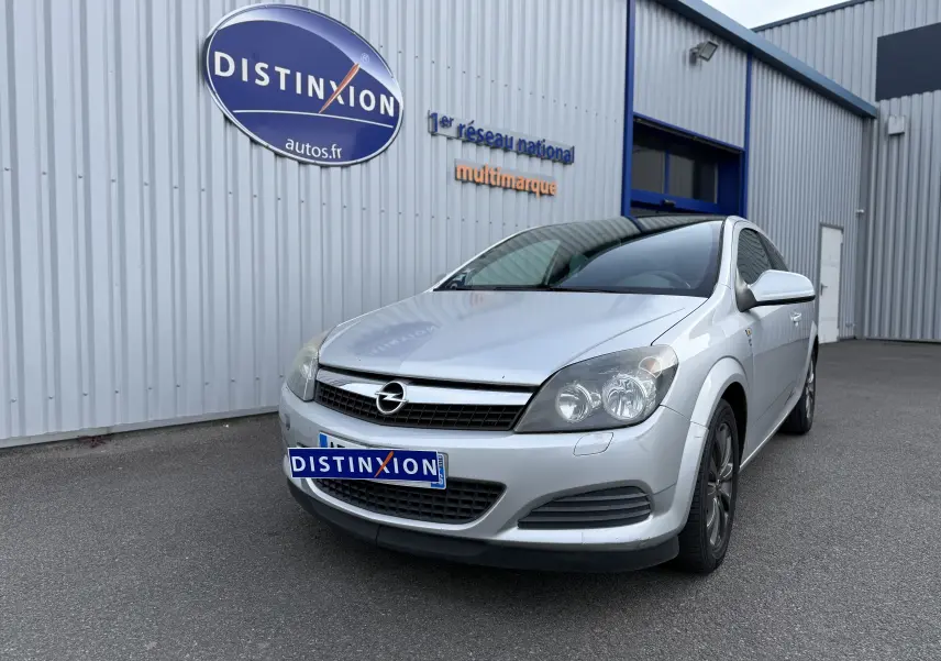 Opel Astra gris vue 3/4 avant droit, garée devant un bâtiment avec panneau Distinxion visible.