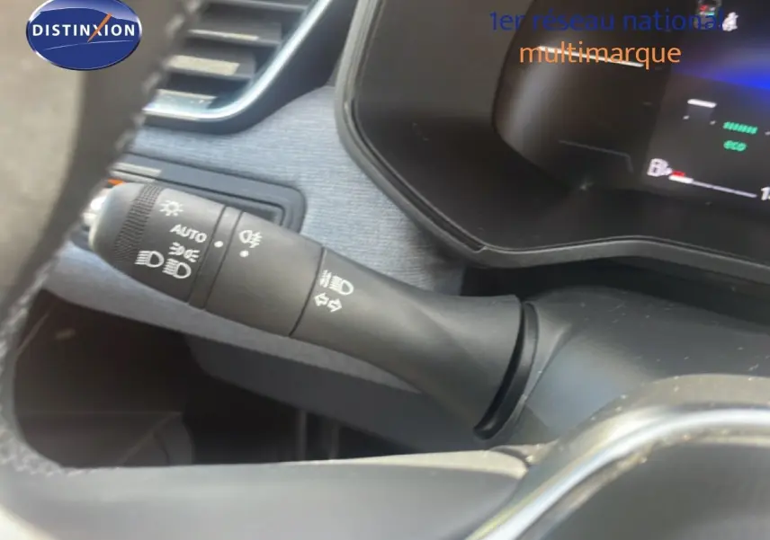 Gros plan sur la commande des feux et clignotants à gauche du volant dans l’habitacle noir de la Renault Clio blanche.