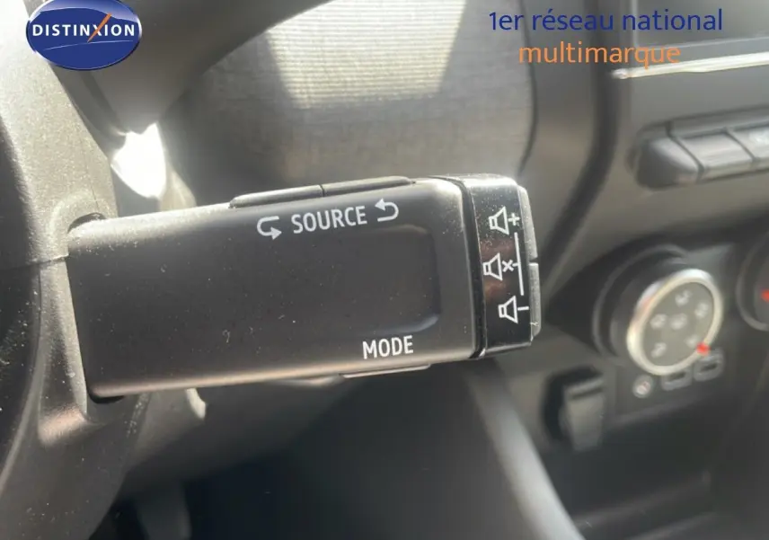 Gros plan sur la commande audio au volant d’une Renault Clio 2025, intérieur noir avec boutons mode et source visibles.