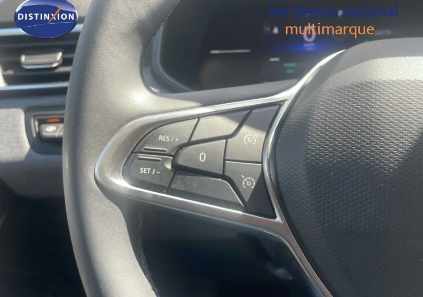 Gros plan sur les commandes au volant côté gauche d'une Renault Clio blanche, mettant en valeur les boutons de régulateur de vitesse.