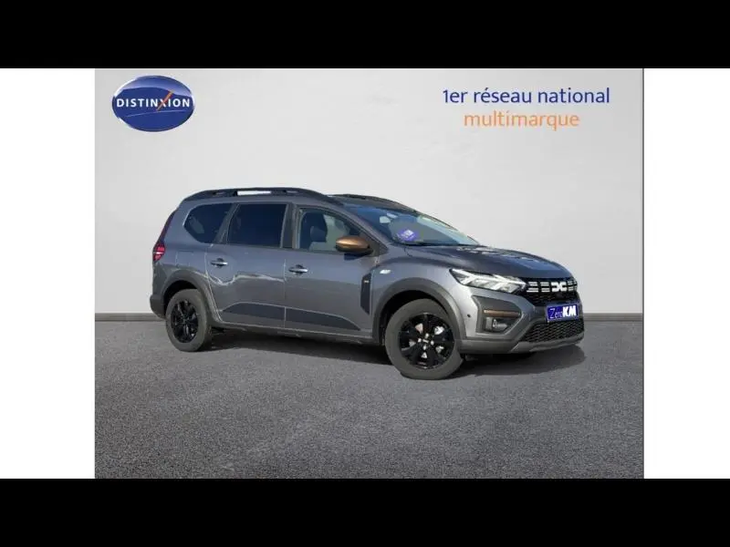 Vue 3/4 avant droit d'un Dacia Jogger gris schiste métallisé avec jantes noires et barres de toit.