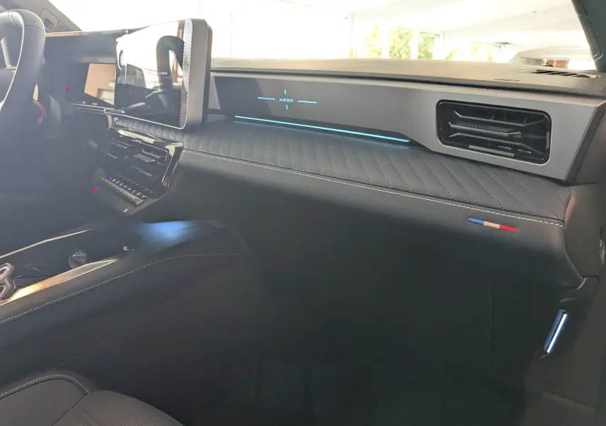 Intérieur de l'Alpine A290 220CH GT Performance vu côté passager, tableau de bord noir avec éclairage bleu et surpiqûres tricolores.
