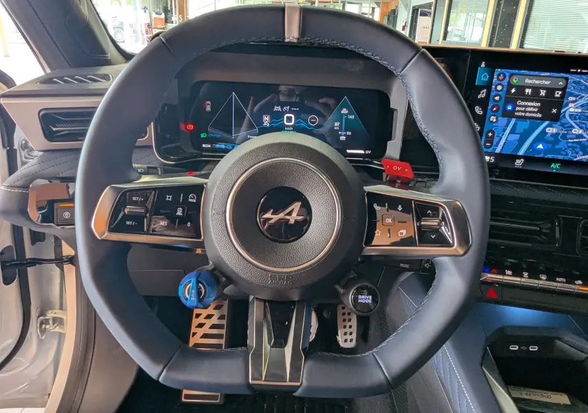 Vue intérieure centrée sur le volant noir de l'Alpine A290 220CH GT PERFORMANCE avec tableau de bord numérique et écran tactile.