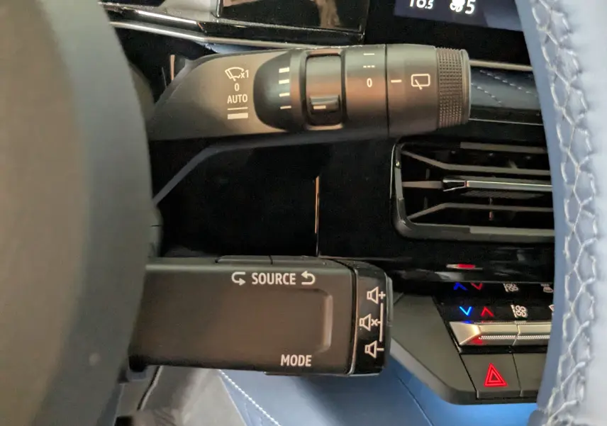Gros plan sur la commande de clignotants et les commandes multimédias à gauche du volant bleu de l'Alpine A290 blanche.