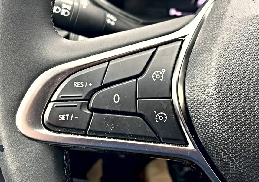 Gros plan sur les commandes de régulateur de vitesse au volant noir de la Renault Clio V blanche.