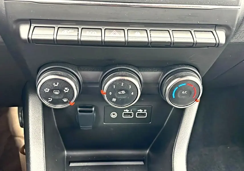 Gros plan sur les commandes de climatisation et les ports USB du tableau de bord d'une Renault Clio V blanche.