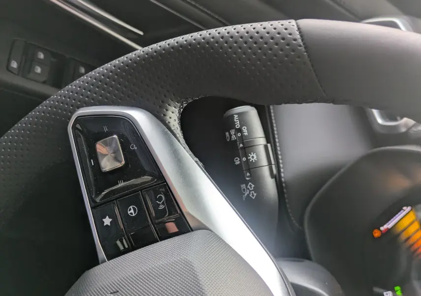 Gros plan sur le volant en cuir perforé noir côté gauche du MG ZS blanc, avec commandes intégrées et tableau de bord numérique visible.
