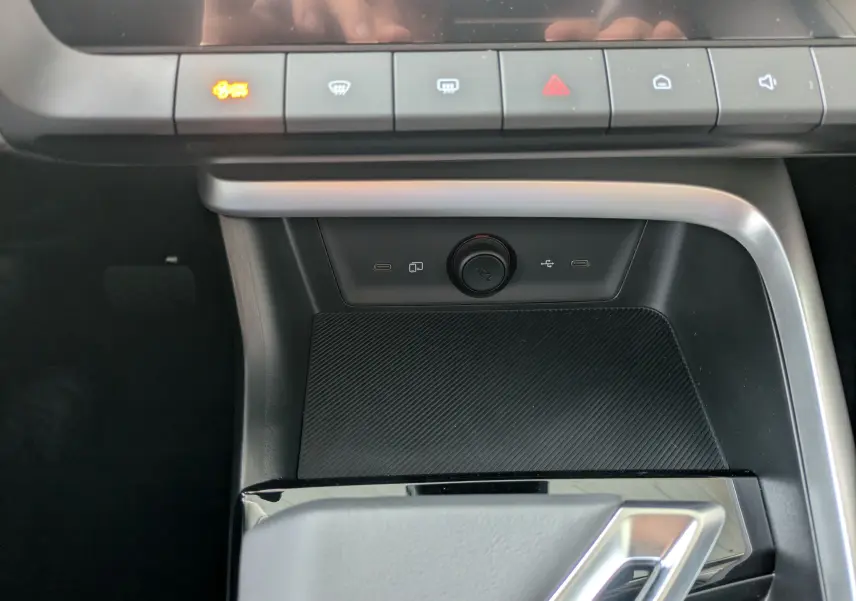 Gros plan sur la console centrale noire du MG MOTOR ZS 1.5 L Hybrid+ 2026, avec boutons de commande et prise USB visibles.