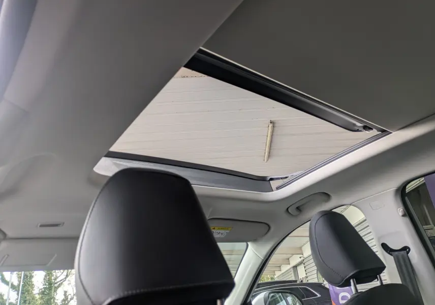 Vue intérieure du toit panoramique ouvert du MG Motor ZS blanc, avec appuis-tête en similicuir noir perforé.