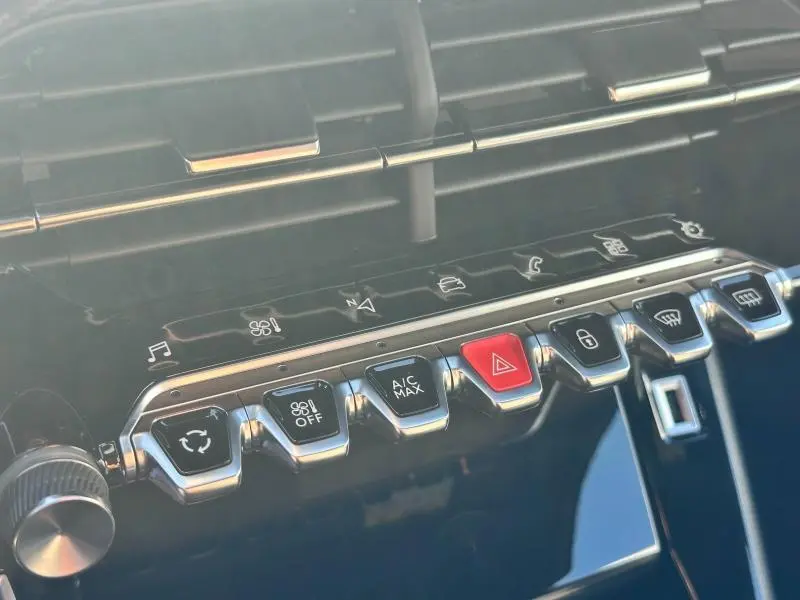Gros plan sur la rangée de boutons chromés du tableau de bord du Peugeot 2008 gris Artense, avec bouton d'alerte rouge.