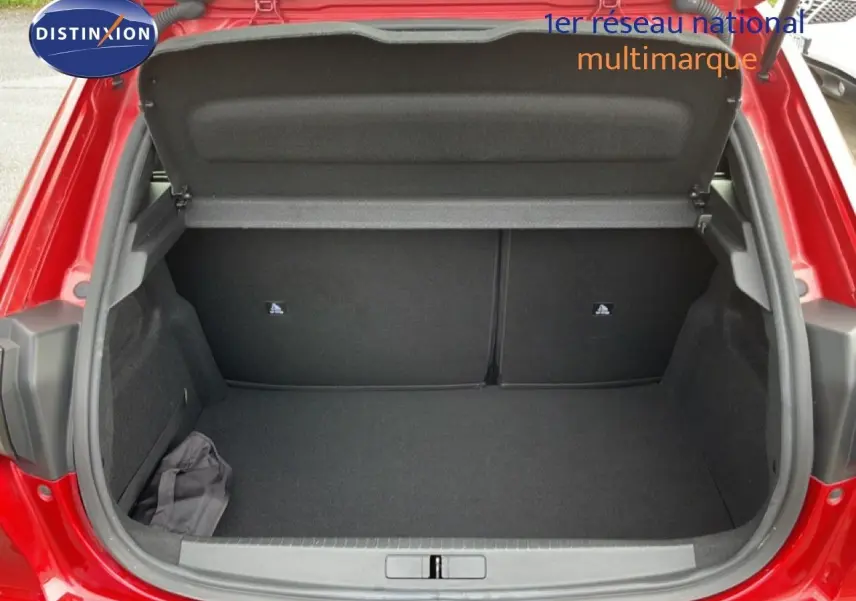 Coffre ouvert vu de l'arrière d'une Peugeot 208 rouge Elixir Metal, montrant un espace de rangement propre et vide.