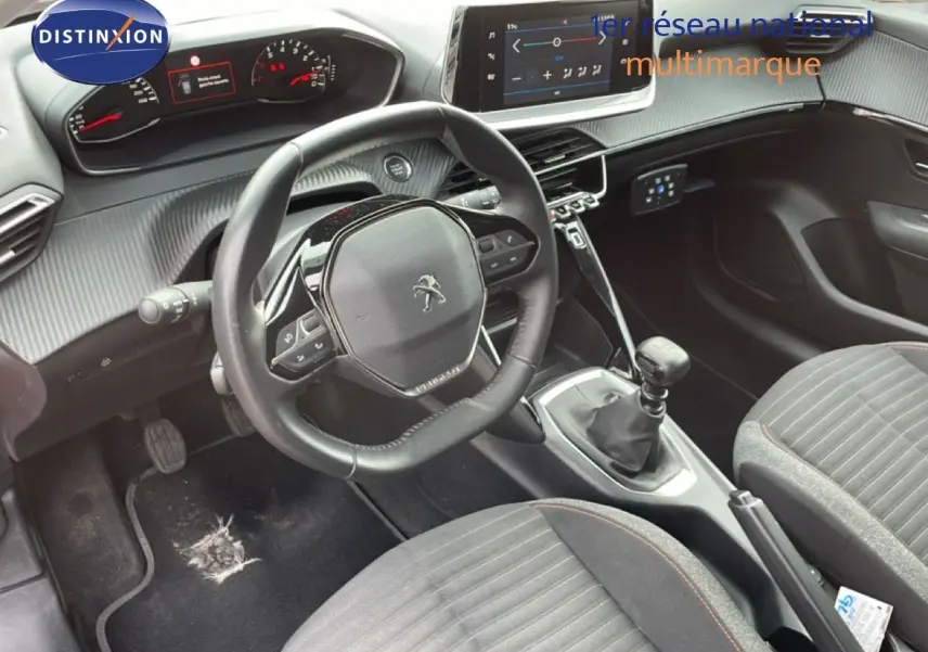 Vue intérieure centrée sur le volant et la console centrale d'une Peugeot 208 rouge Elixir, boîte manuelle visible.