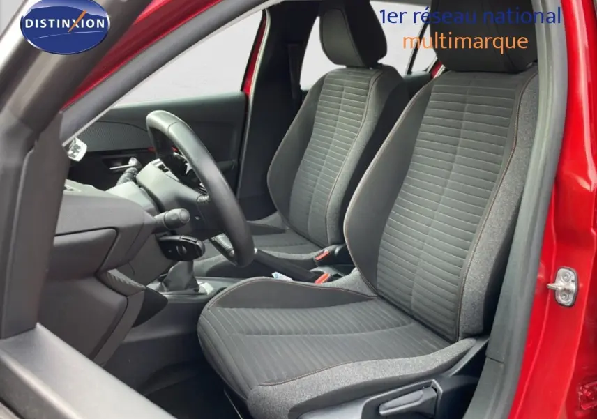 Vue intérieure côté conducteur de la Peugeot 208 rouge Elixir Metal, montrant les sièges tissu noir et gris et le volant.