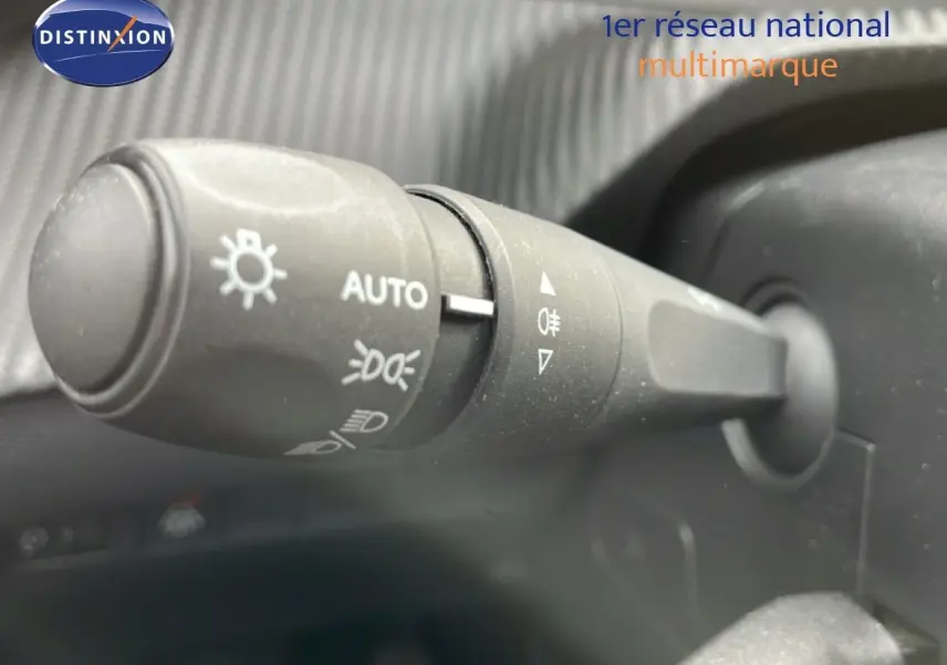 Gros plan sur la manette de commande des phares à gauche du volant dans l’habitacle d’une Peugeot 208 rouge Elixir Metal.