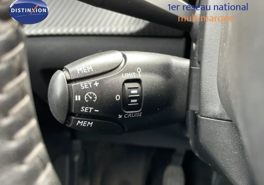 Gros plan sur la commande de régulateur de vitesse noire dans l'habitacle d'une Peugeot 208 rouge Elixir Metal.
