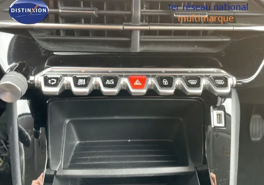 Gros plan sur la console centrale noire brillante de la Peugeot 208 rouge, avec rangée de boutons chromés et port USB visible.
