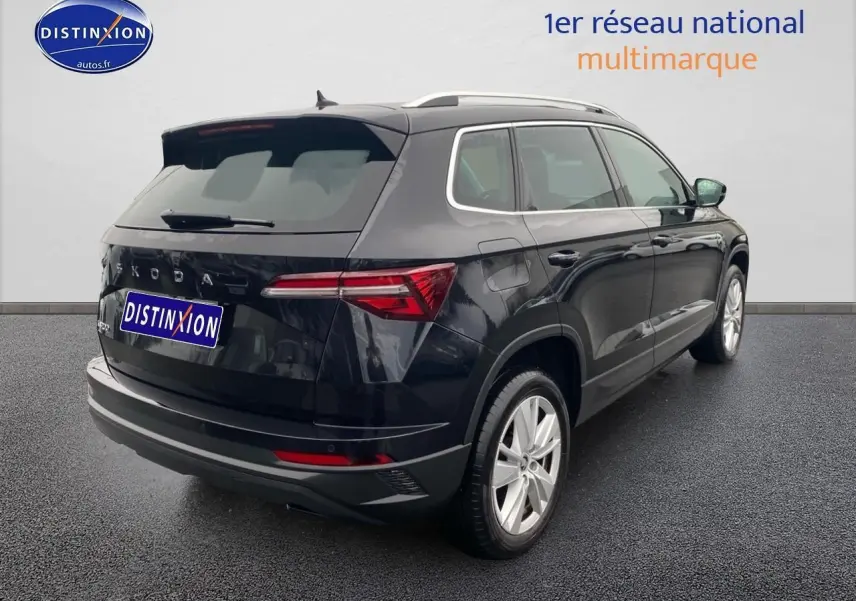 Vue 3/4 arrière droite d'un Skoda Karoq noir 2025 avec jantes alu et barres de toit argentées.