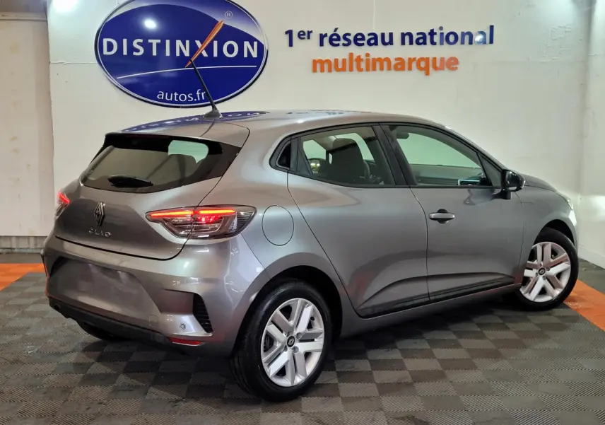 Vue 3/4 arrière droite d'une Renault Clio gris foncé Evolution Blue dCi 100, feux arrière allumés en intérieur showroom.
