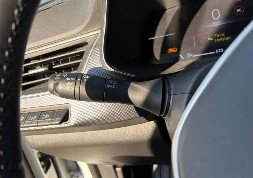 Détail intérieur du commodo d'éclairage à gauche du volant dans un Renault Arkana blanc Glacier 2025.