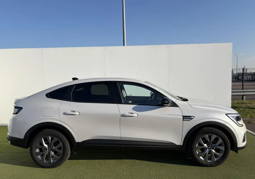 Profil droit d’un Renault Arkana blanc glacier 2025 avec jantes alliage grises et vitres surteintées.