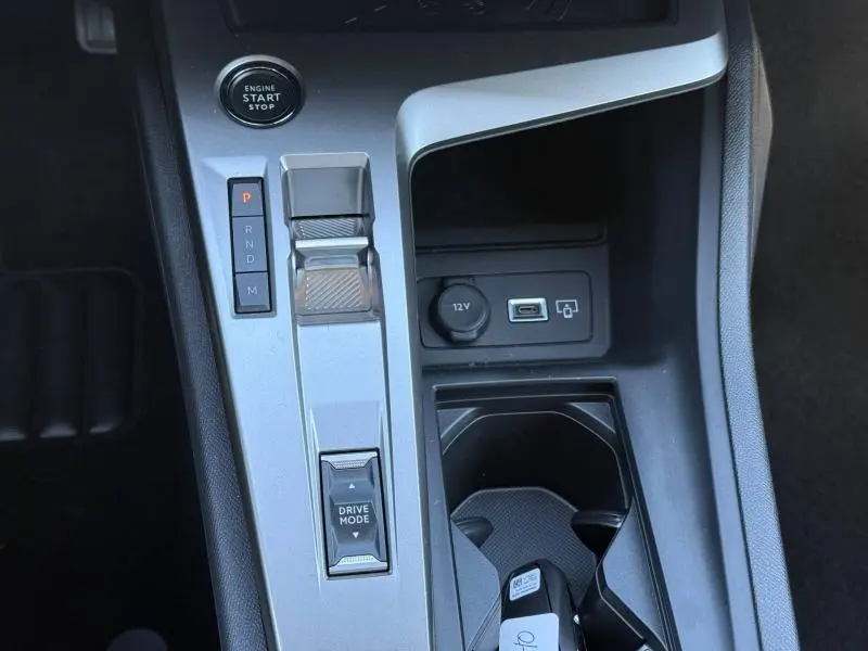 Vue rapprochée de la console centrale grise du Peugeot 308 Hybrid 2025, avec bouton start, sélecteur de boîte auto et prise 12V.