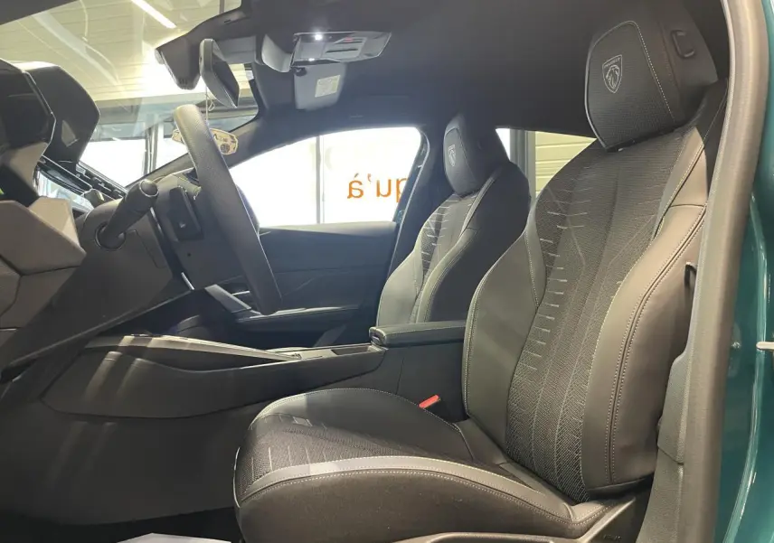 Vue intérieure côté droit de la Peugeot 308 2026, sièges tissu noir avec surpiqûres et logo Peugeot brodé.
