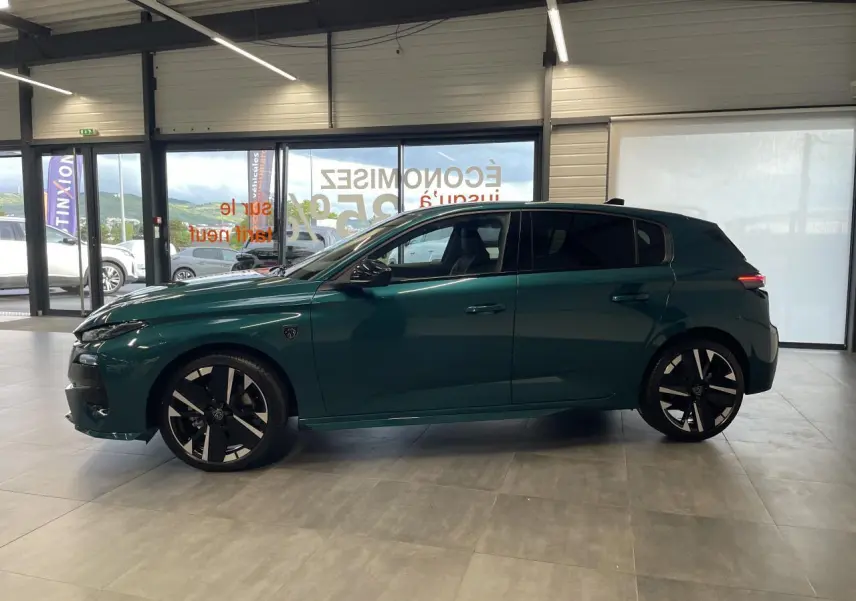 Profil droit de la Peugeot 308 GT bleu métallisé avec jantes alliage bi-tons et vitres surteintées en showroom.