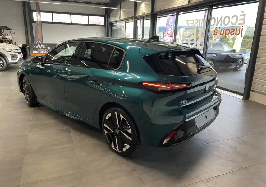 Peugeot 308 bleu métallisé vue 3/4 arrière droit en intérieur avec jantes alliage bi-tons et feux LED allumés.