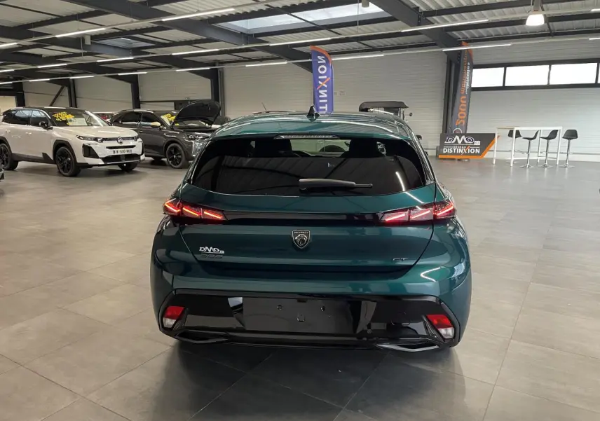 Vue arrière d'une Peugeot 308 GT bleu métallisé avec feux arrière 3 griffes LED et bandeau noir brillant en showroom.