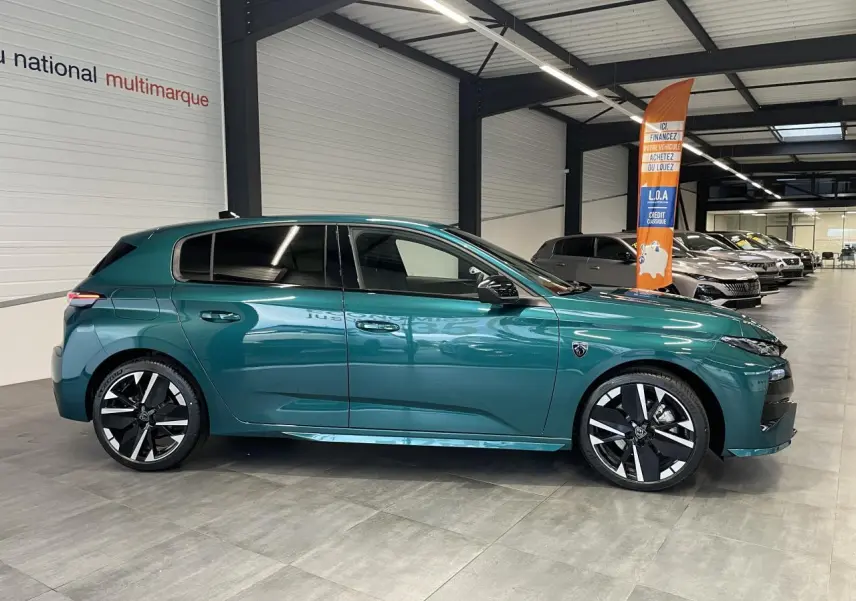 Vue latérale droite d'une Peugeot 308 GT 2026 bleu métallisé avec jantes alliage bi-tons et vitres surteintées en showroom.