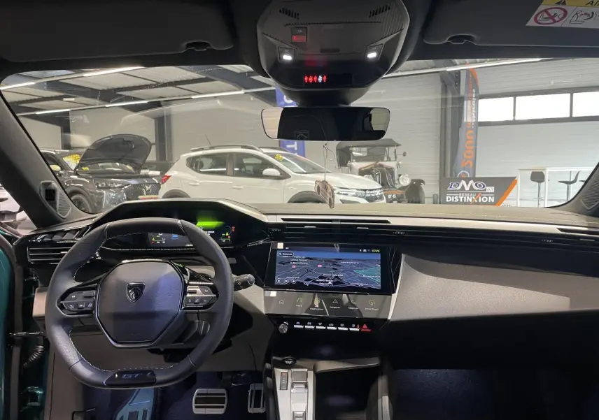 Vue intérieure avant du Peugeot 308 bleu, mettant en valeur le volant GT compact, l'écran tactile central et les pédaliers aluminium.