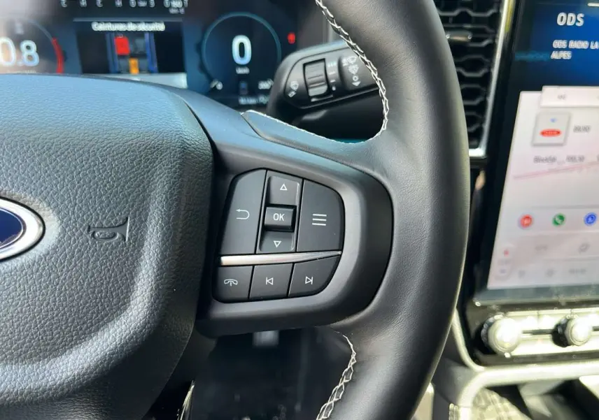 Gros plan sur le volant cuir noir du Ford Ranger 2026 avec commandes multifonctions et écran tactile visible à droite.