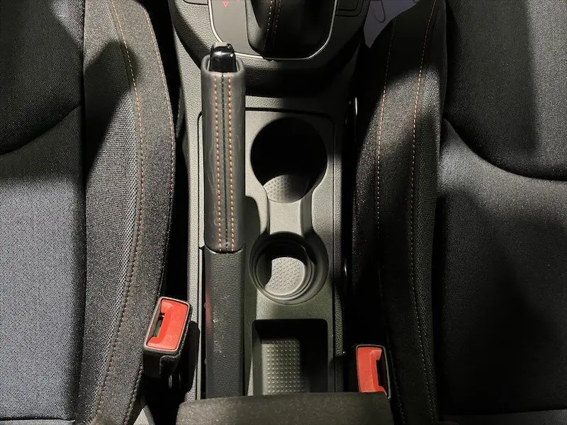 Vue plongeante sur la console centrale noire de la SEAT IBIZA 2024, avec frein à main et porte-gobelets entre sièges tissu noir.