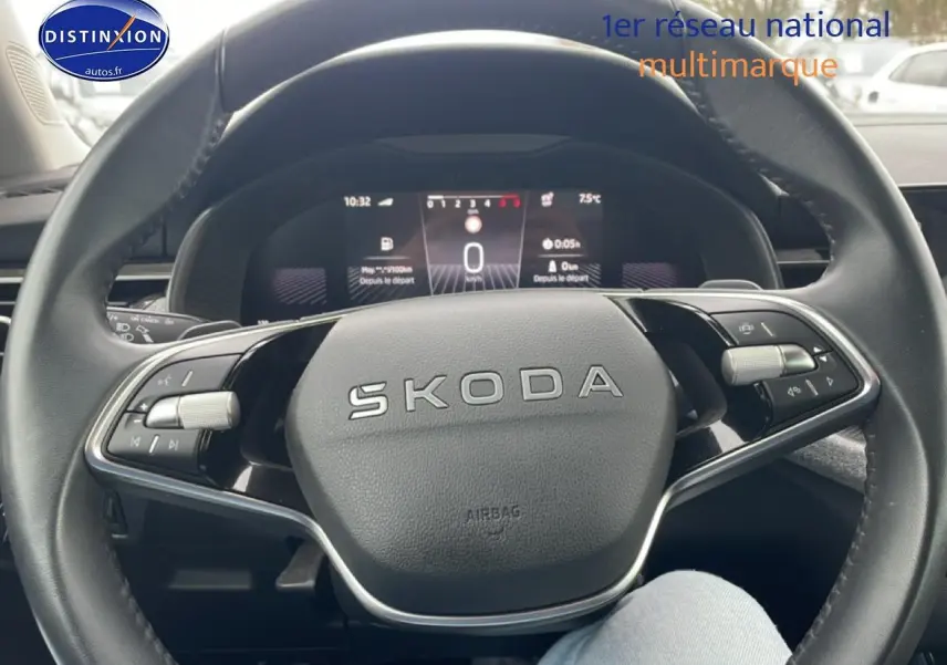 Vue rapprochée du volant cuir noir SKODA avec commandes multifonctions et tableau de bord numérique en arrière-plan.