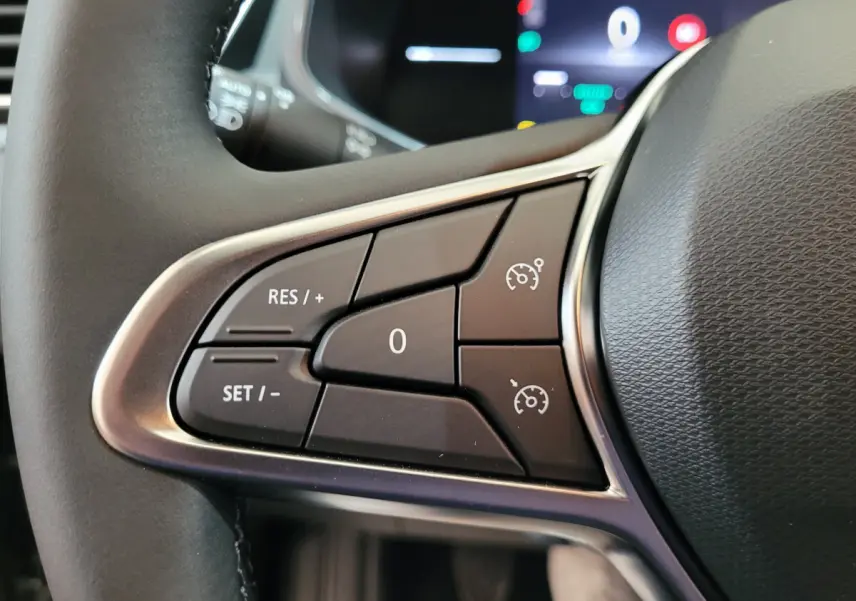 Gros plan sur les commandes du régulateur de vitesse au volant cuir de la Renault Clio gris foncé, tableau de bord en arrière-plan flou.