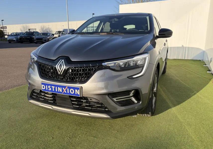 Renault Arkana gris métallisé vu de face droite, avec calandre noire et phares LED distinctifs.