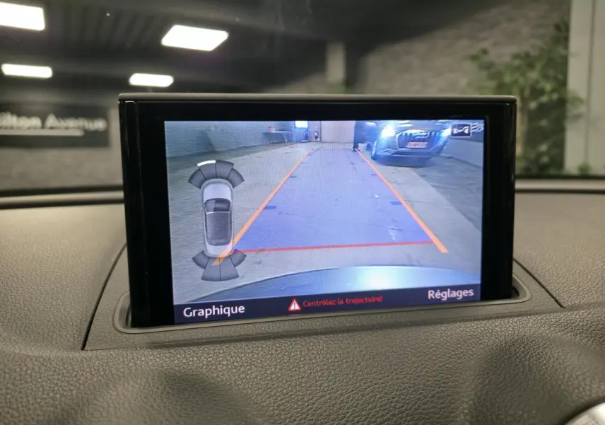 Écran de caméra de recul affichant la zone derrière l'Audi A3 Cabriolet gris, avec lignes de guidage orange et rouge.