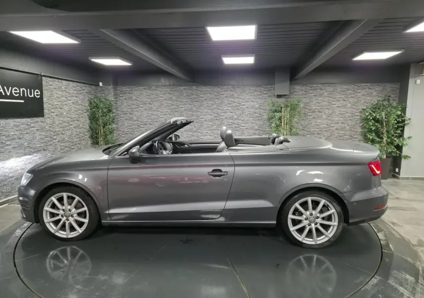Audi A3 Cabriolet gris en profil droit, capote ouverte, jantes 10 branches et feux arrière allumés.